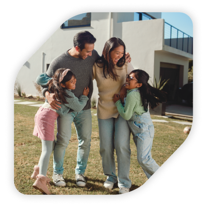 A couple and two children embrace on the lawn of a home